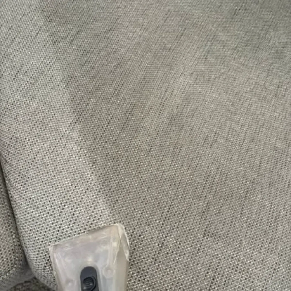 Professional upholstery cleaning tool on grey woven sofa fabric