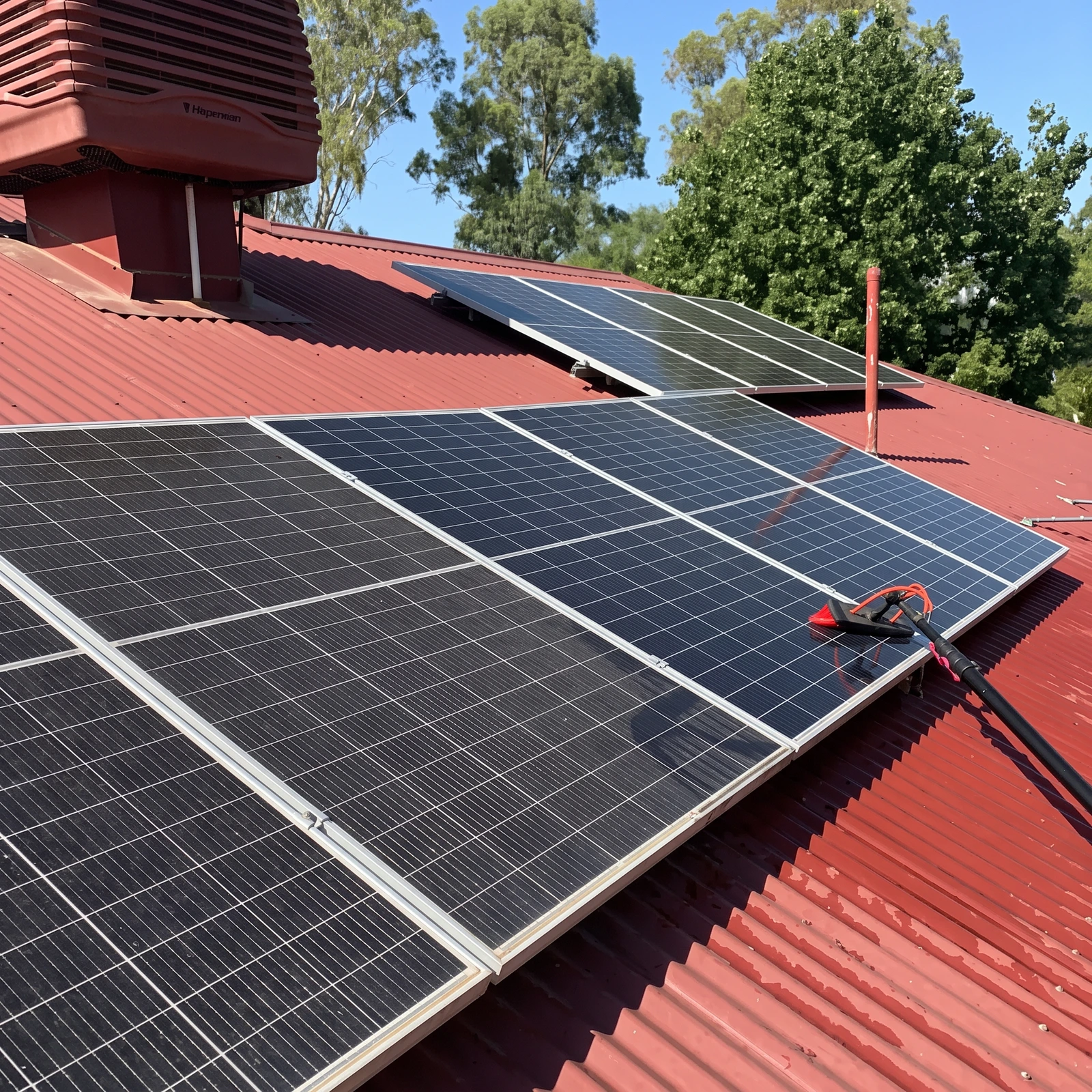 Solar panels being professionally cleaned by Shepp City Carpet Cleaning on red iron roof with cleaning tool visible