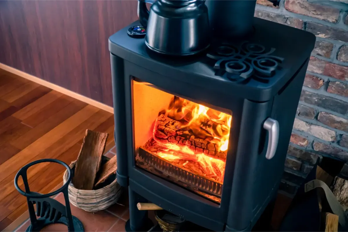 Wood fire heater with flames visible through glass door beside brick wall